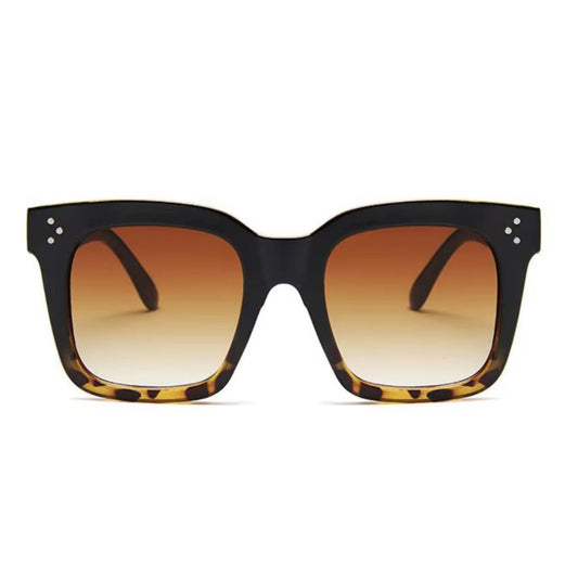 Oversized square sunglasses with a black-to-tortoiseshell frame, gradient brown lenses, and subtle metal rivet details on the corners for a chic and bold look.